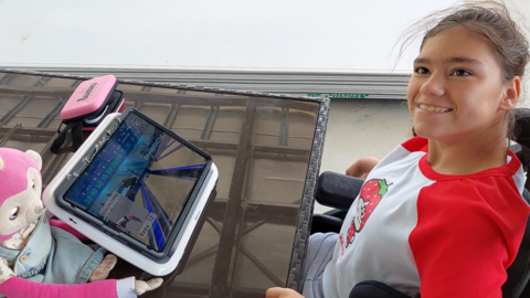 A girl in a wheelchair smiling while playing a LusioMATE game on a tablet
