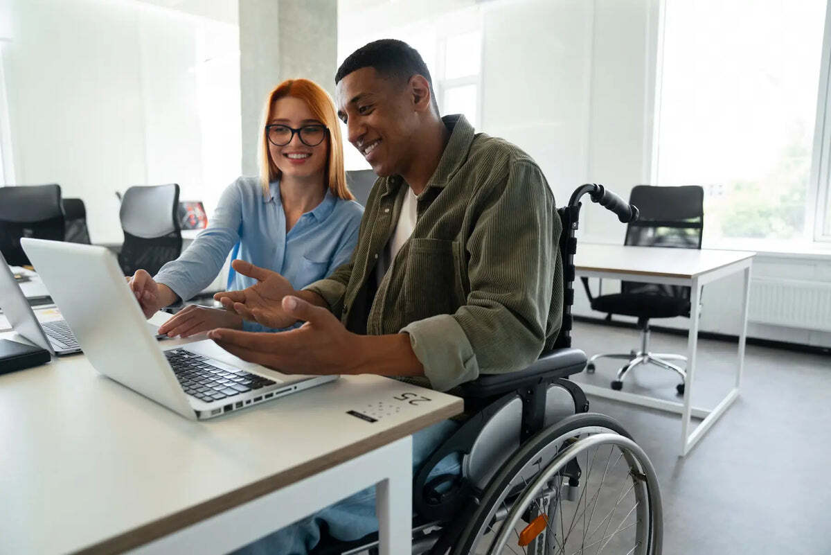 A wheelchair user and a colleague looking at a laptop together