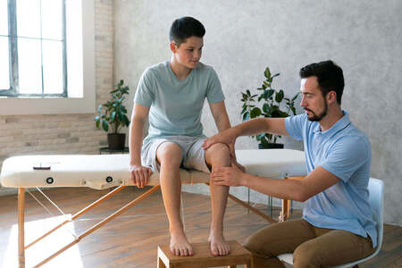 A physiotherapist examining a boy's knee on a treatment table
