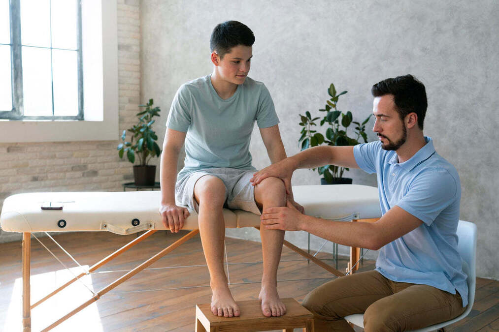 A physiotherapist examining a boy's knee on a treatment table