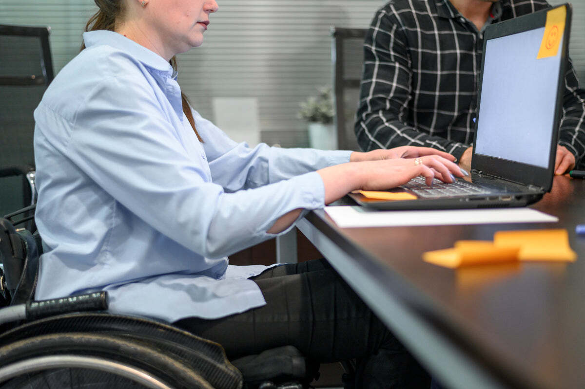 A woman in a wheelchair typing on a laptop at a desk