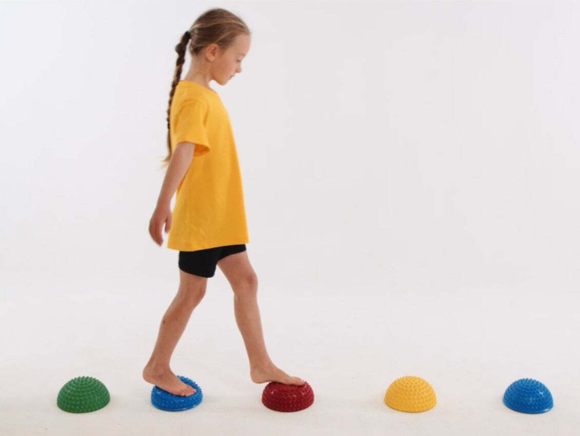 A child walking barefoot across coloured balance domes