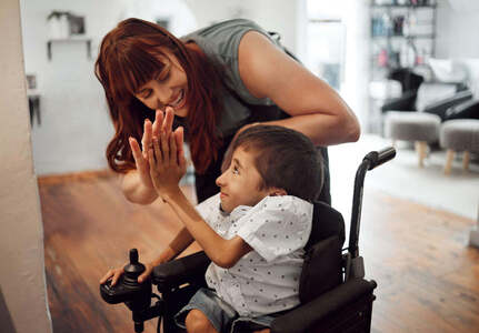A woman high-fiving a boy in a powered wheelchair at home