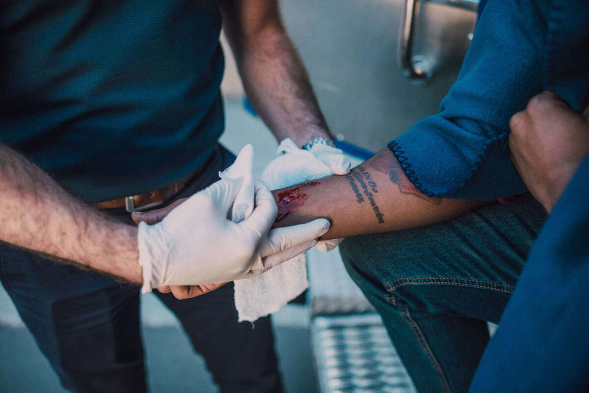 Someone applying gauze to a bleeding forearm injury