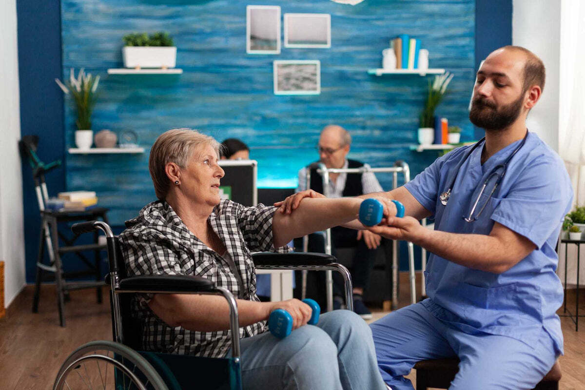 A physiotherapist helping a woman in a wheelchair lift a hand weight
