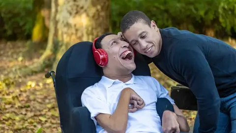 A man in a wheelchair laughing with a friend outdoors
